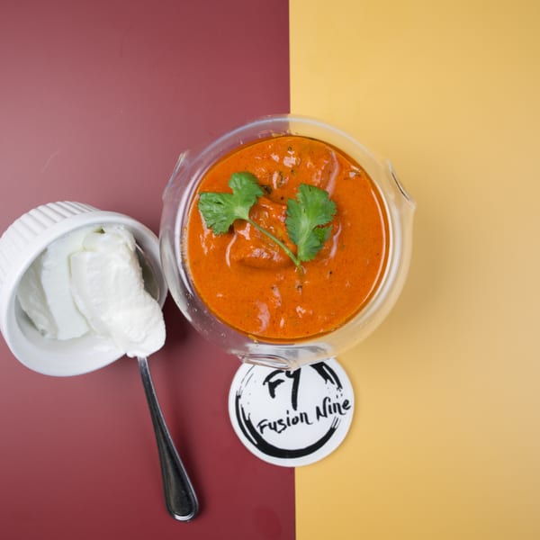 Overhead view of a glass bowl of orange curry with cilantro, next to a white bowl of cream.