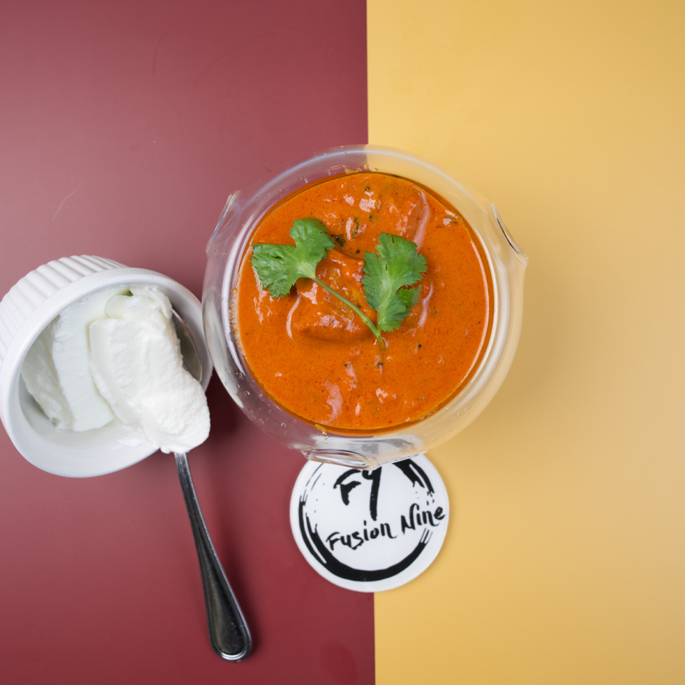 Overhead view of a glass bowl of orange curry with cilantro, next to a white bowl of cream.