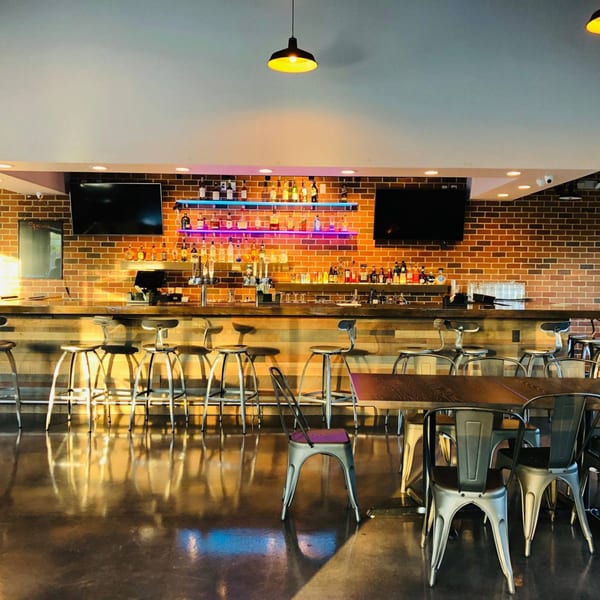 The bar area at Fusion Nine, featuring a brick wall, wooden bar, and colorful neon lights.
