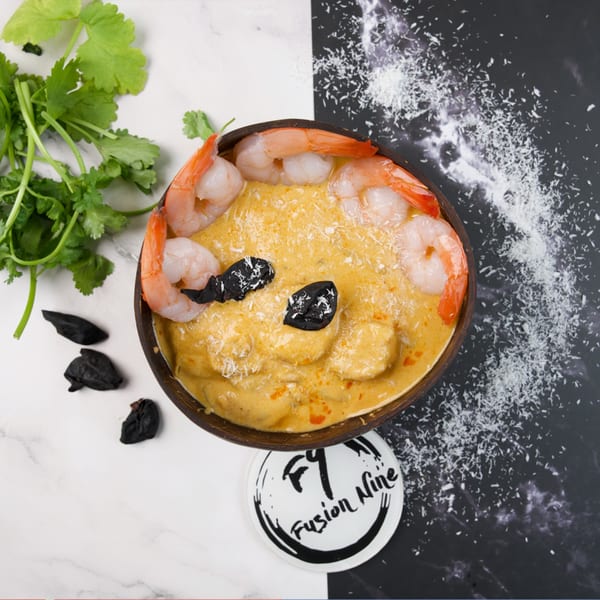Shrimp curry in a coconut bowl with cilantro, black garlic, and shredded coconut on a split background.