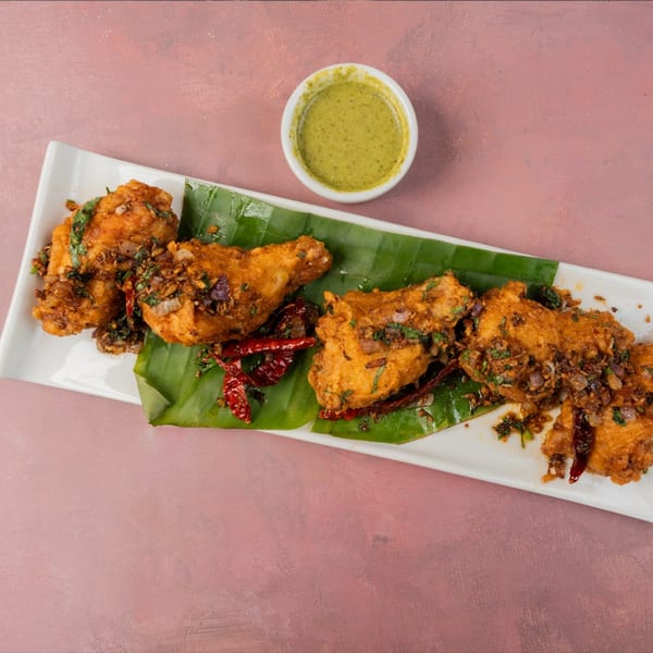 Fried chicken drumsticks with herbs, spices, and dried chilies on banana leaves, served with green chutney.