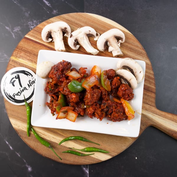 Spicy red chicken dish with bell peppers and onions, garnished with mushrooms and green chilies.