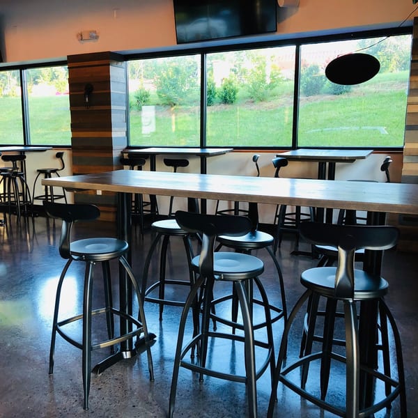 Interior of Fusion Nine, an Indian restaurant, with tall tables, bar stools, and large windows overlooking greenery.