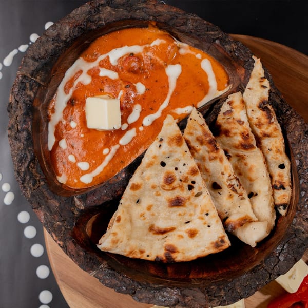 Butter chicken with naan bread served in a rustic wooden bowl on a dark background.