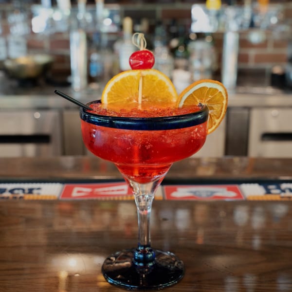 A vibrant red margarita with orange slices and a cherry on a bar counter.