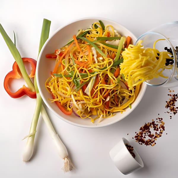 Indian noodles with vegetables, red bell pepper, and green onions on a white surface.