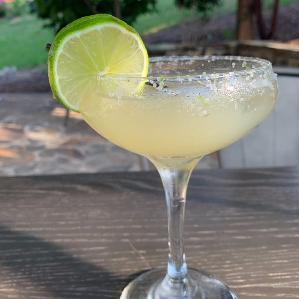 A margarita in a stemmed glass with a lime slice and salted rim on a wooden table.