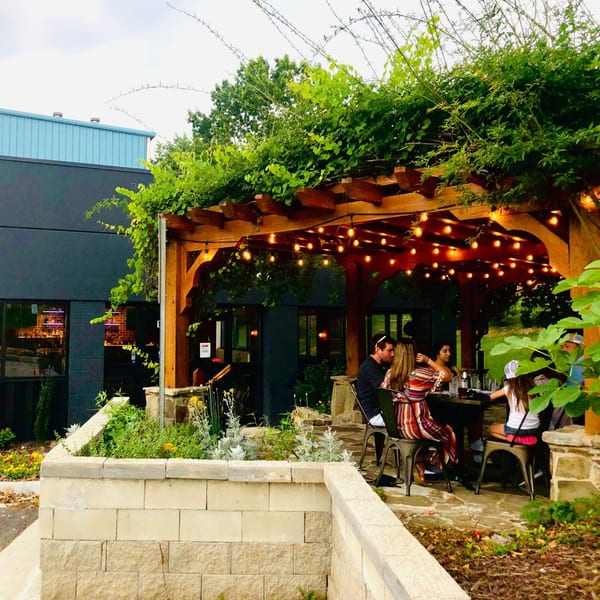 Patrons dining outdoors under a vine-covered pergola with string lights at Fusion Nine.