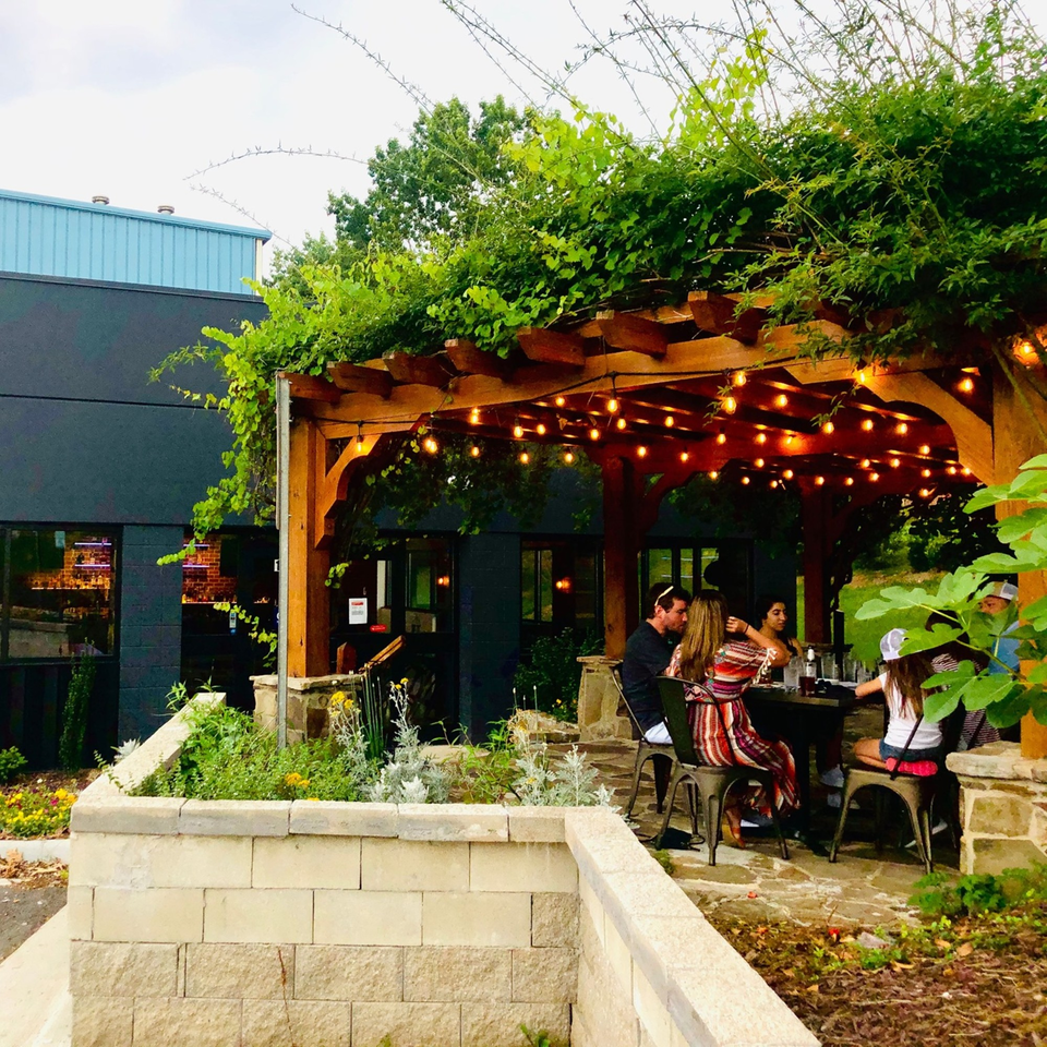 Patrons dining outdoors under a vine-covered pergola with string lights at Fusion Nine.