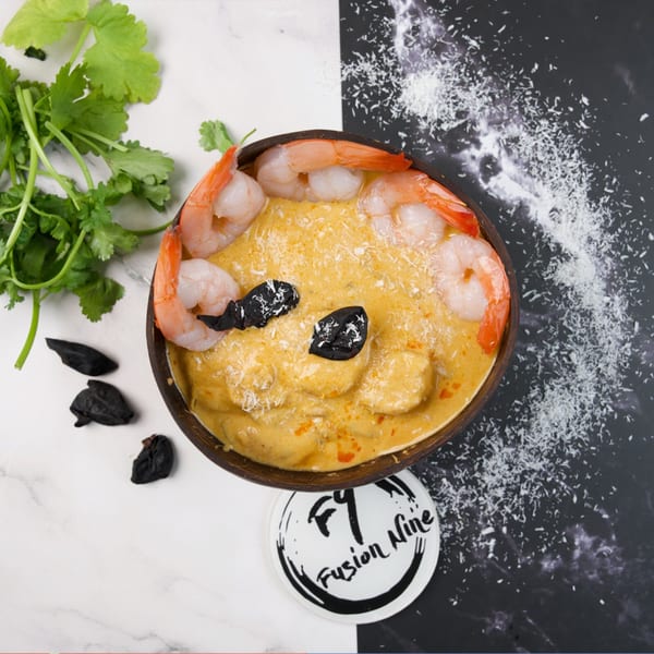 Shrimp curry in a coconut bowl with cilantro, black garlic, and shredded coconut on a split background.