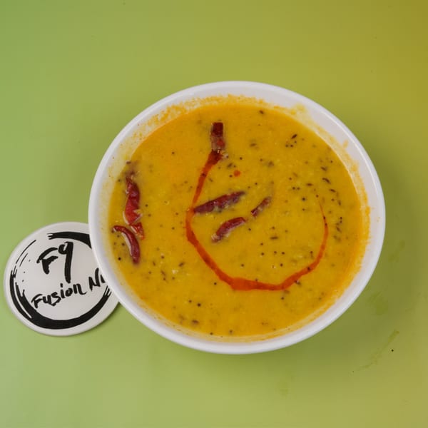 A bowl of yellow lentil soup with red chili oil and dried red chilies on a green background.