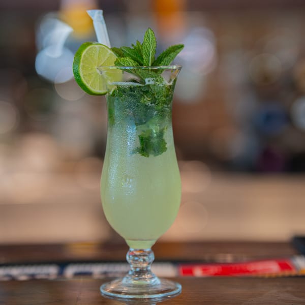 A refreshing mojito cocktail with lime and mint in a tall glass on a wooden bar.