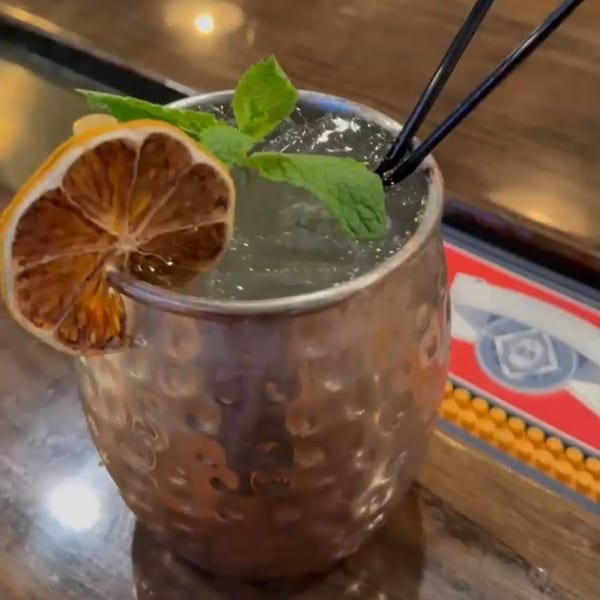 A Moscow Mule cocktail in a hammered copper mug, garnished with a dried orange slice and fresh mint.