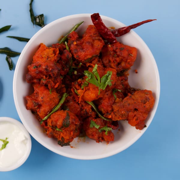 A white bowl filled with vibrant red fried chicken, garnished with green chilies and cilantro.