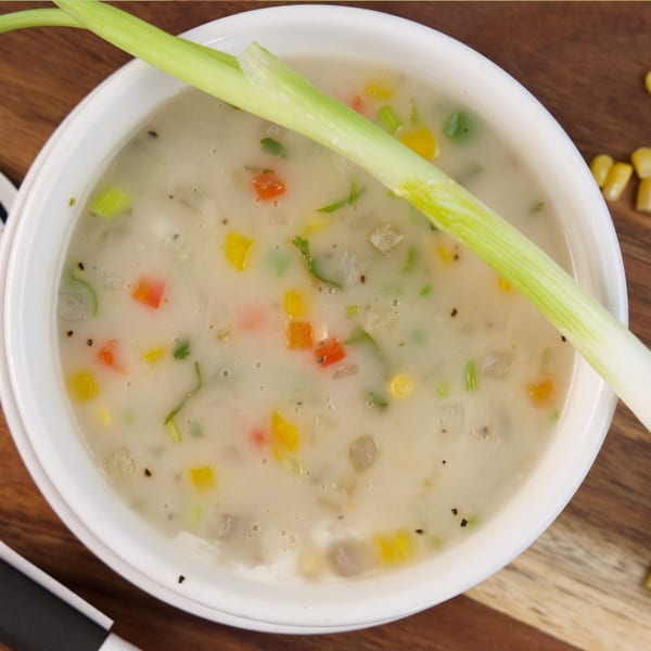 Creamy vegetable soup in a white bowl, garnished with a fresh green onion stalk.