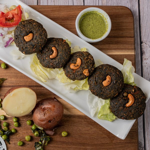 Dark brown patties topped with cashews, served on lettuce with a side of green sauce.