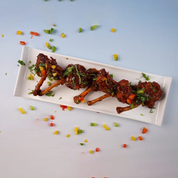 Chicken lollipops with sauce and chopped bell peppers on a white rectangular plate.