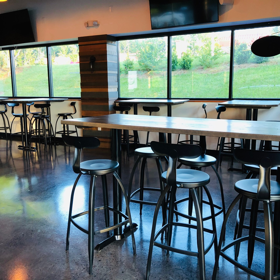 Modern dining area at Fusion Nine with tall tables, black bar stools, and large windows overlooking a green lawn.