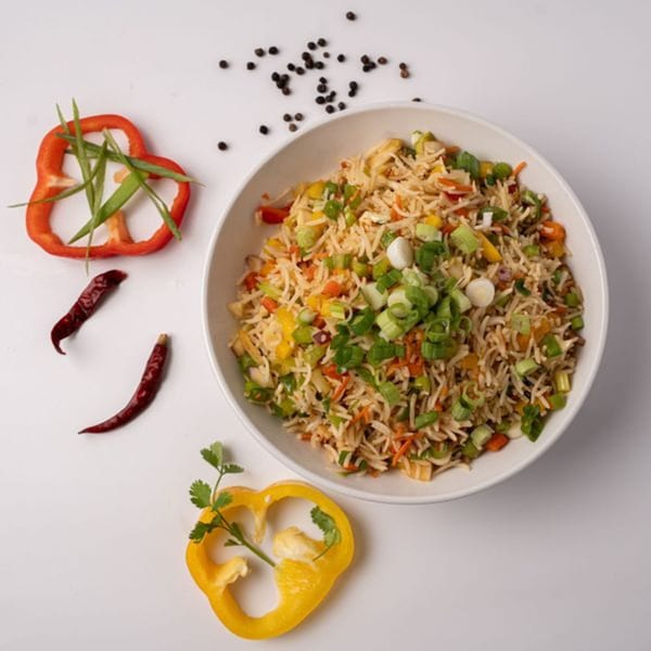 A white bowl of colorful vegetable fried rice, garnished with green onions, bell peppers, and chilies.