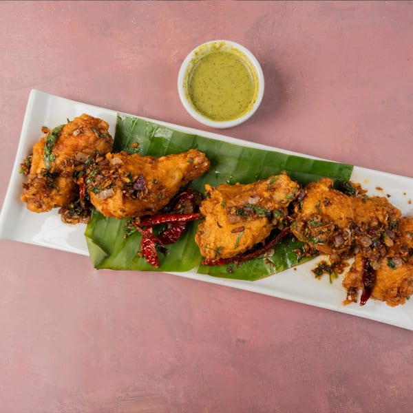 Crispy fried chicken drumsticks with herbs, spices, and dried chilies on banana leaves, with green chutney.