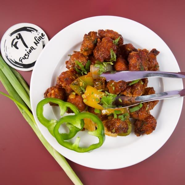 Fusion Nine's chili chicken with bell peppers and cilantro, served with tongs and green onions.