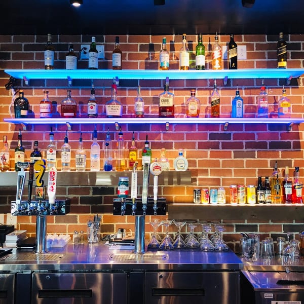 A well-stocked bar at Fusion Nine with various liquor bottles, beer taps, and glassware against a brick wall.